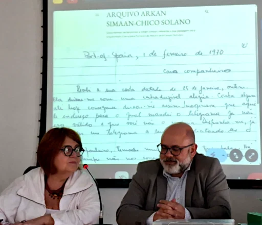 Bárbara Corrales e Edmar Macedo no ato de doação do acervo de Arkan Simaan. Na tela uma das cartas